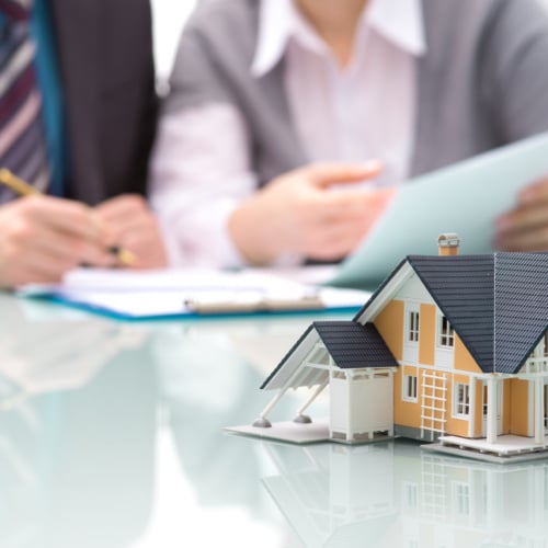 Image of home architectural model on a table with two people sitting at the table one signing a document.