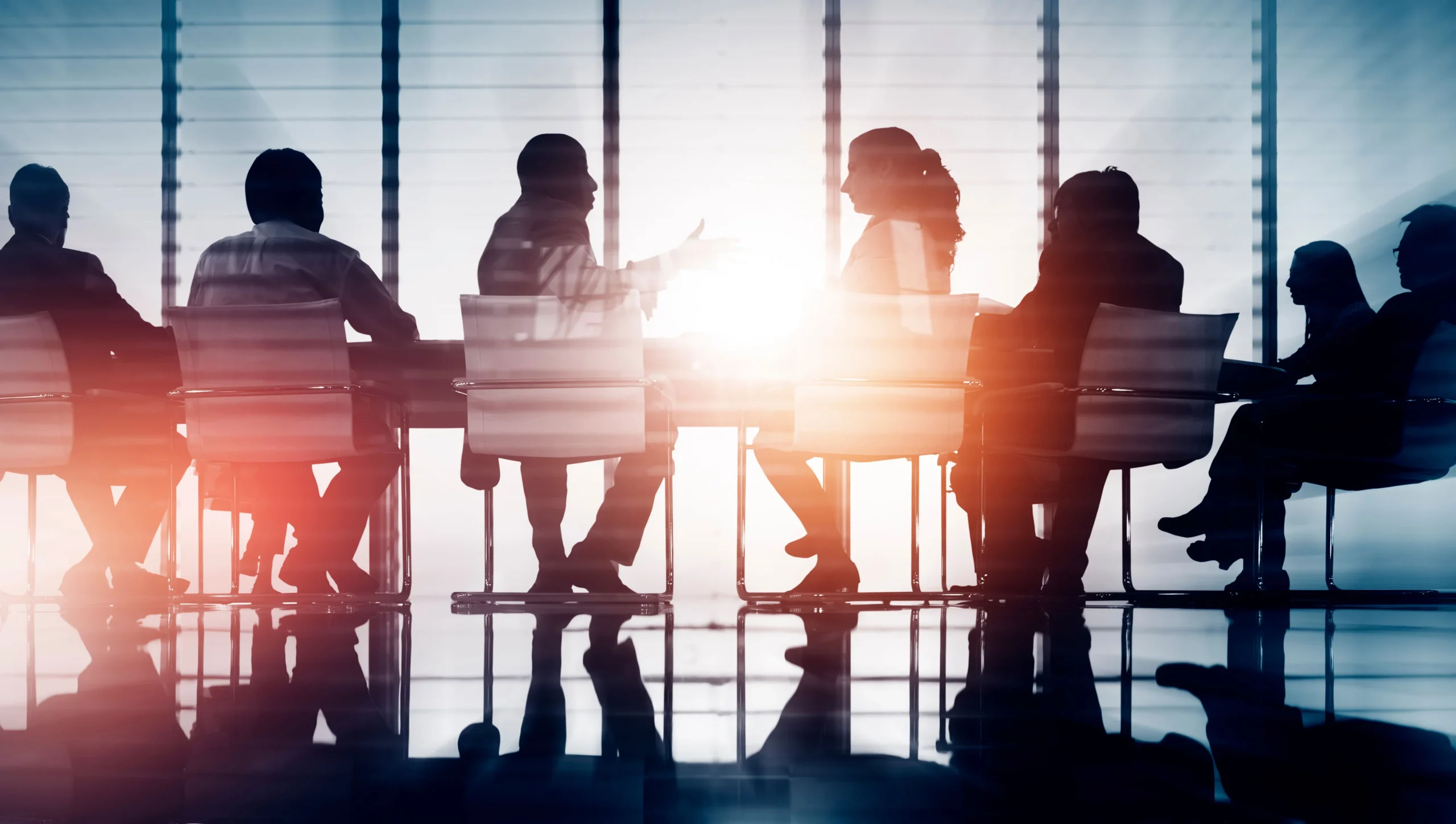 View of a business team talking in a glass boardroom with the sunset illuminating their silhouettes, representing the business and corporate commercial lawyers at EKB law firm in Vancouver, BC